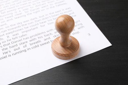 One wooden stamp and sheet of paper with text on black table, closeupの写真素材