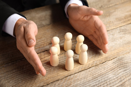 Man protecting human figures at wooden table, closeupの写真素材