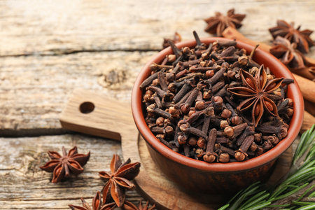 Mulled wine spices. Cloves in bowl, anise stars and fresh rosemary on wooden table, closeup. Space for textの写真素材