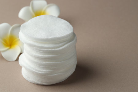 Stack of clean cotton pads and plumeria flowers on beige background, closeup. Space for textの写真素材
