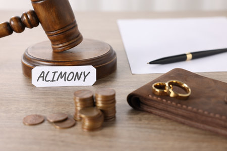 Paper note with word Alimony, judge's gavel, coins, wallet, wedding rings, pen and document on wooden table, closeupの写真素材