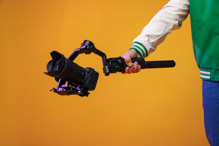 Videographer using gimbal stabilizer with camera on yellow background, closeupの写真素材