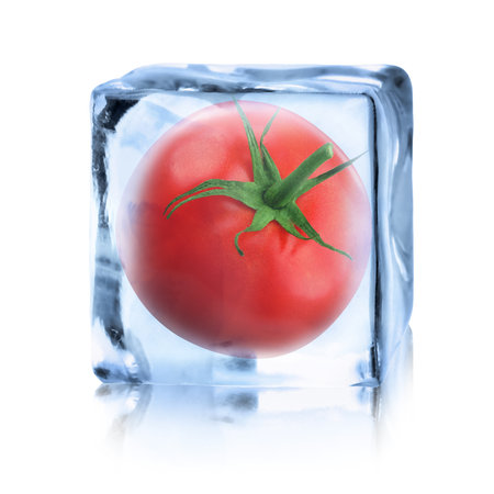 Whole red tomato in ice cube inside isolated on whiteの写真素材