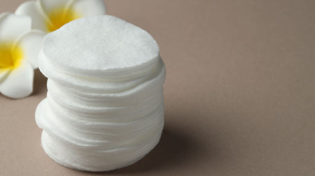 Stack of clean cotton pads and plumeria flowers on beige background, closeup. Space for textの写真素材