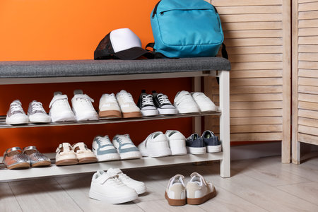 Different kid's shoes, storage bench and folding screen near orange wall indoorsの写真素材