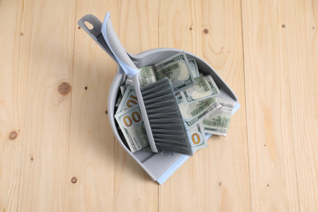 Dustpan with broom and dollar banknotes on wooden background, top viewの写真素材