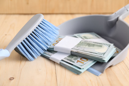 Dustpan with broom and dollar banknotes on wooden background, closeupの写真素材