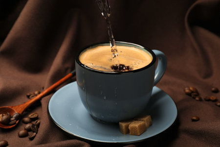 Pouring aromatic coffee into cup, beans and brown sugar on fabric, closeupの写真素材