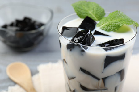 Glass of milk with tasty herbal jelly and mint on table, closeup. Space for textの写真素材