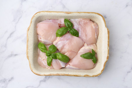 Raw chicken thighs with basil in baking dish on white marble table, top viewの写真素材