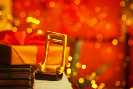 Christmas atmosphere. Golden music note and gift box on piano against red background with blurred lights, closeup with space for text. Bokeh effectの写真素材