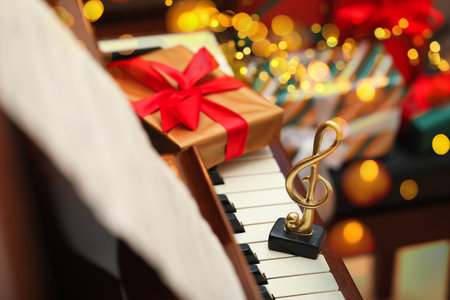 Christmas atmosphere. Golden treble clef and gift box on piano against blurred lights, closeup. Bokeh effectの写真素材