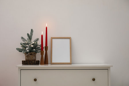 Christmas decor, frame and burning candles on cabinet near white wall indoorsの写真素材