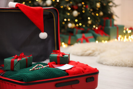 Christmas vacation. Suitcase with Santa hat, clothes, candy canes and gift boxes on floor indoors, closeupの写真素材
