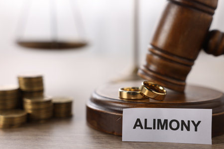 Paper note with word Alimony, wedding rings, judge's gavel and coins on wooden table, closeupの写真素材