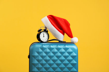 Christmas vacation. Blue suitcase with Santa hat and alarm clock on orange backgroundの写真素材