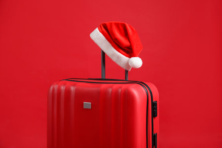 Christmas vacation. Suitcase with Santa hat on red backgroundの写真素材