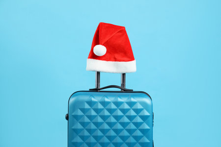 Christmas vacation. Suitcase with red Santa hat on light blue backgroundの写真素材