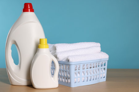 Laundry basket with clean towels and detergents on wooden table against light blue background, space for textの写真素材