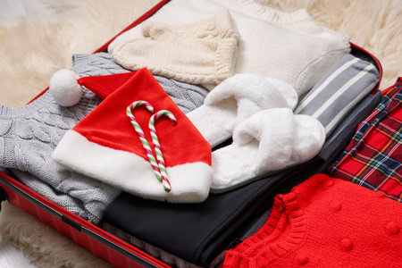 Christmas vacation. Suitcase with Santa hat, clothes and candy canes on floor indoors, closeupの写真素材
