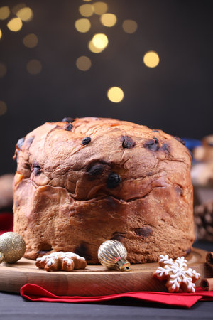 Christmas food. Delicious Panettone cake, gingerbread cookies and decor on black wooden table against blurred lights, closeup. Bokeh effectの写真素材