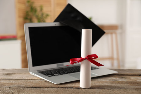 Diploma, graduation hat and laptop on wooden table indoors, selective focusの写真素材