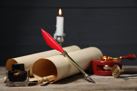 Old paper scroll, fountain pen, inkwell, wax seal and burning candle on wooden table. Space for textの写真素材