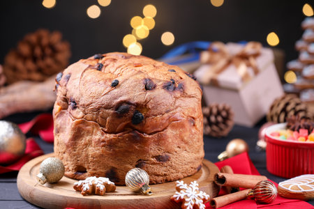 Christmas food. Delicious Panettone cake, gingerbread cookies, candied fruits and decor on black wooden table against blurred lights, closeup. Bokeh effectの写真素材