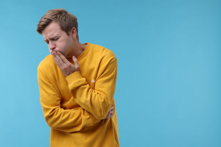 Young man suffering from nausea and stomachache on light blue background, space for textの写真素材