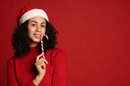 Beautiful woman with Santa hat and candy cane on red background, space for text. Christmas seasonの写真素材