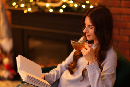 Woman with tea reading book near fireplace at homeの写真素材