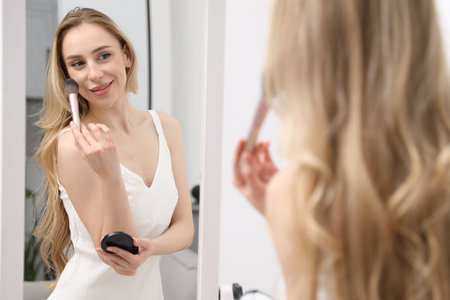 Beautiful woman applying makeup near mirror indoorsの写真素材