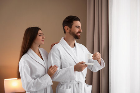 Happy couple in bathrobes with morning coffee indoorsの写真素材