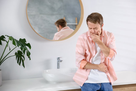 Young man suffering from nausea and stomachache in bathroomの写真素材