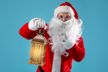 Santa Claus with lantern showing silence gesture on light blue background. Merry Christmas and Happy New Yearの写真素材