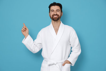 Man in bathrobe pointing at something on light blue backgroundの写真素材