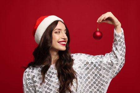 Charming woman wearing Santa hat with Christmas tree ornament on red backgroundの写真素材