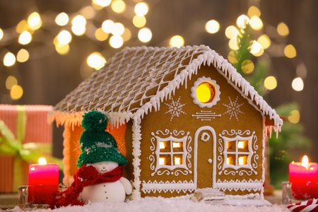 Beautiful gingerbread house and Christmas decor on table against blurred lights, closeup