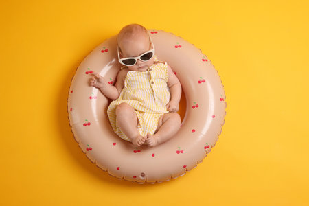 Cute little baby with sunglasses on inflatable ring against orange background, top viewの写真素材
