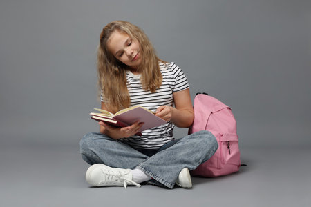 Cute girl with books and backpack on gray backgroundの写真素材