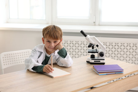 Smiling little boy with microscope writing at desk indoors. Child and scienceの写真素材