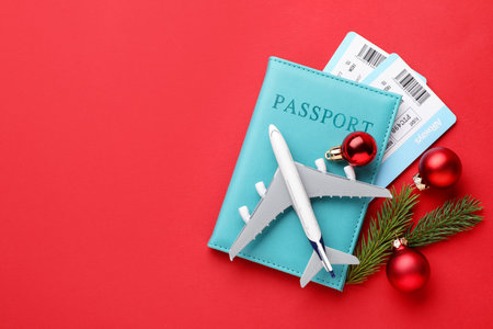Christmas vacation. Passport with tickets, toy plane, fir branches and baubles on red background, flat lay. Space for textの写真素材