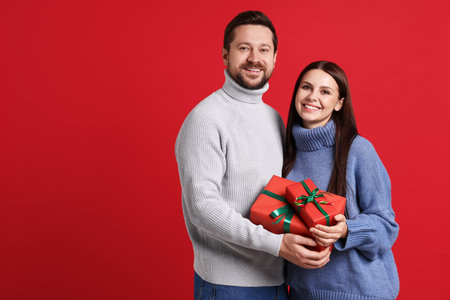 Happy couple with Christmas gifts on red background. Space for textの写真素材