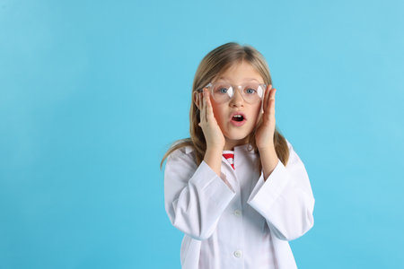 Emotional little girl in laboratory coat and glasses on light blue background, space for text. Child and scienceの写真素材