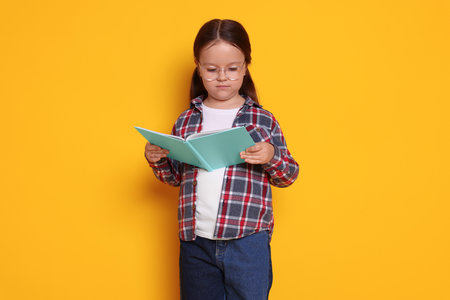 Cute little girl reading book on orange backgroundの写真素材