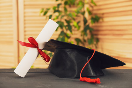Diploma and graduation hat on grey wooden table indoors, closeup. Space for textの写真素材