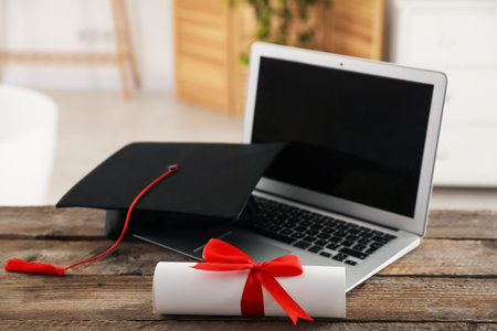 Diploma, graduation hat and laptop on wooden table indoors, selective focusの写真素材