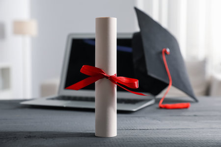 Diploma, graduation hat and laptop on gray wooden table indoors, selective focusの写真素材