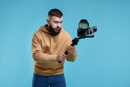 Videographer using gimbal stabilizer with camera on light blue background