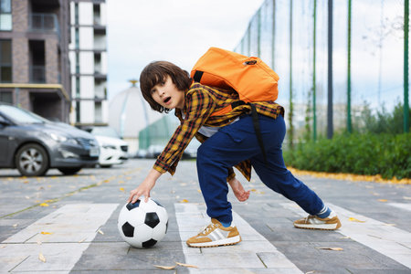 Little boy with backpack catching ball on pedestrian crossing outdoors. Child in danger and road safetyの写真素材